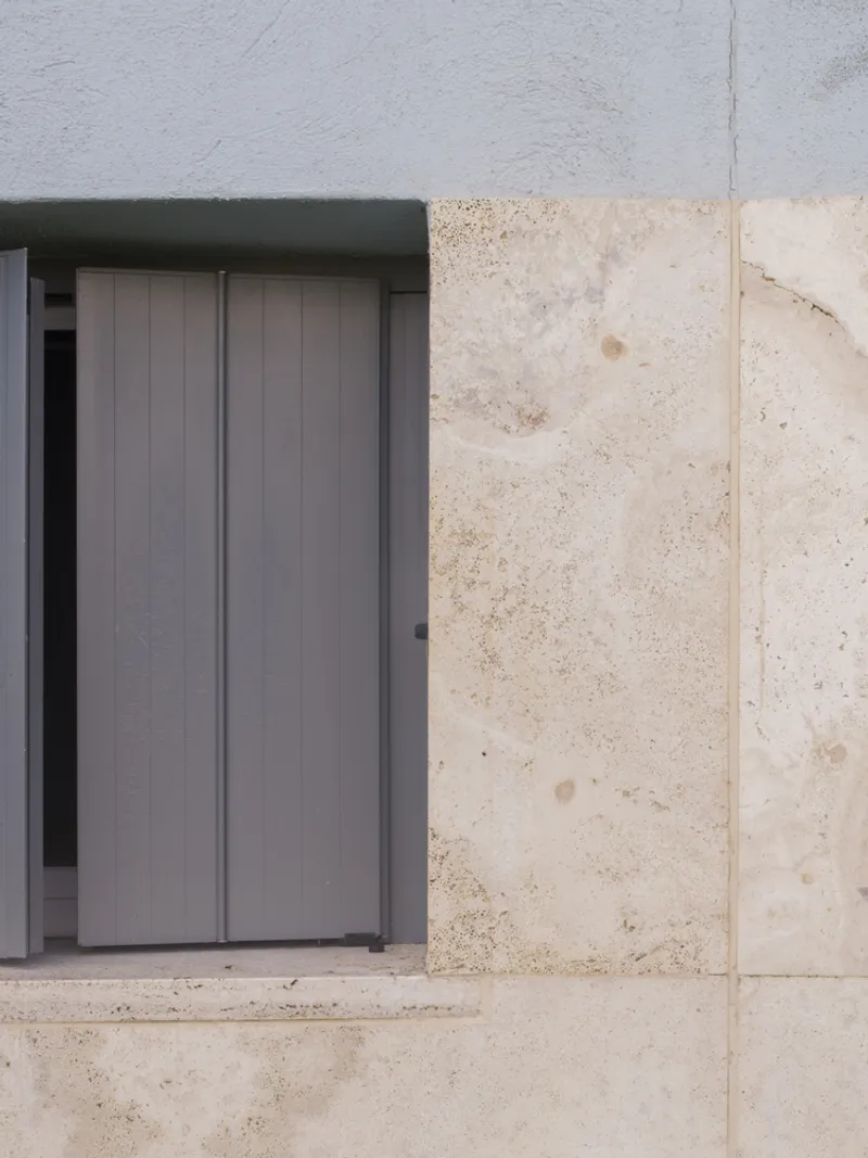 Close-up of grey metal door frame set into pale stone wall with visible construction joints