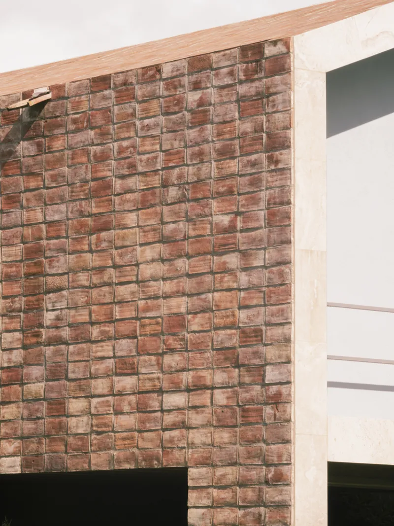 Interior corner detail showing basket-weave terracotta tile wall meeting timber ceiling beam and white plaster surface
