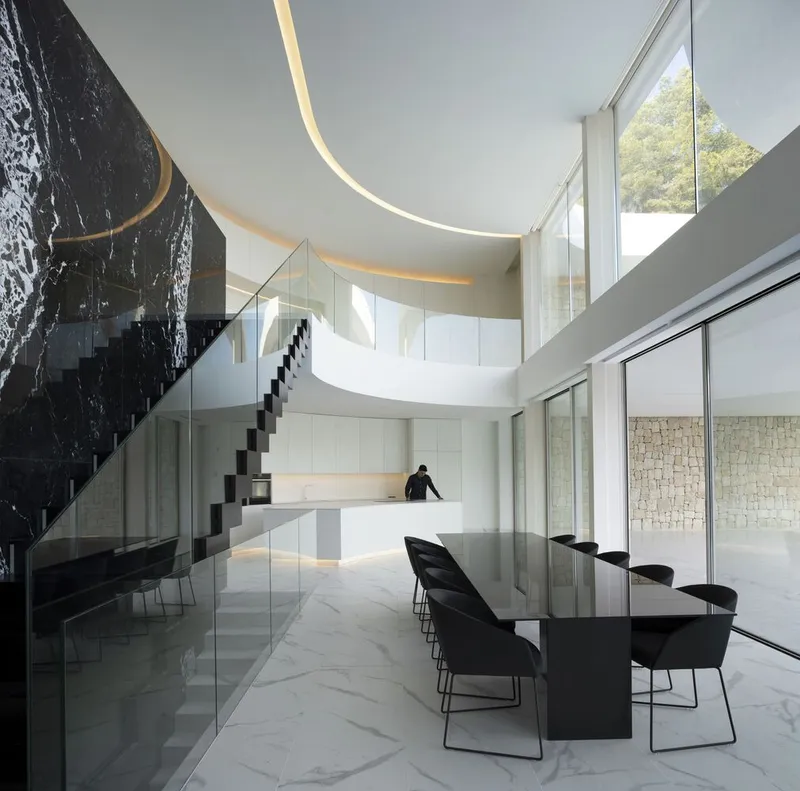 Double-height dining area with cantilevered staircase, curved ceiling, and textured black stone wall