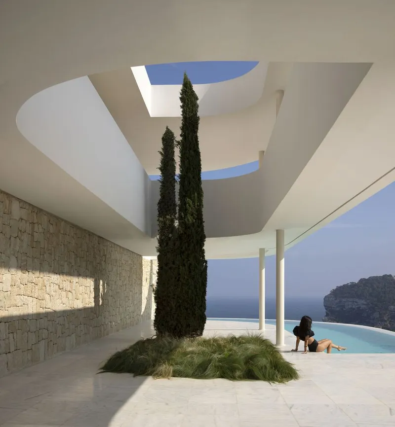 Covered courtyard with cypress tree rising through sculptural ceiling openings beside a pool