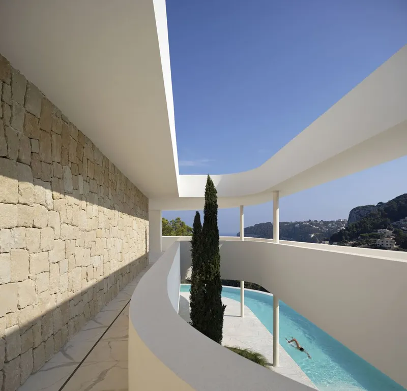 Upper-level terrace with stone wall and cypress tree framing a lap pool below