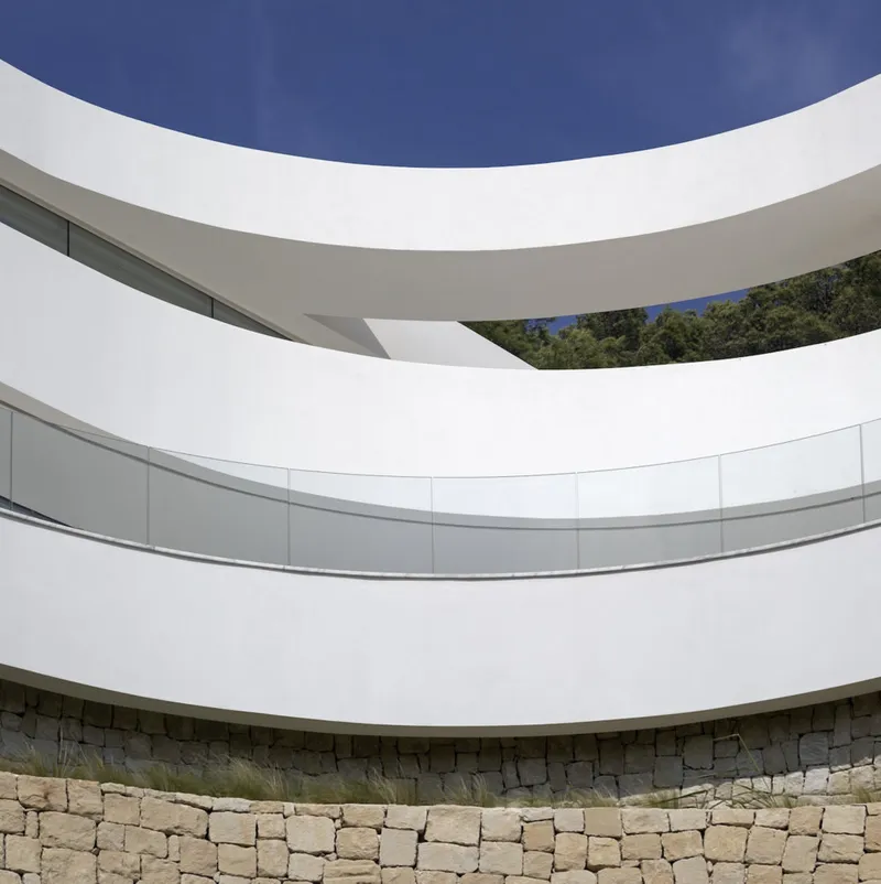 Stacked white balconies with curved parapets above a dry-stacked stone retaining wall