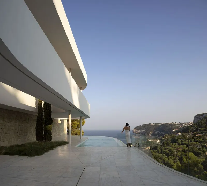 Infinity pool terrace with glass balustrade overlooking the sea as a figure walks at sunset