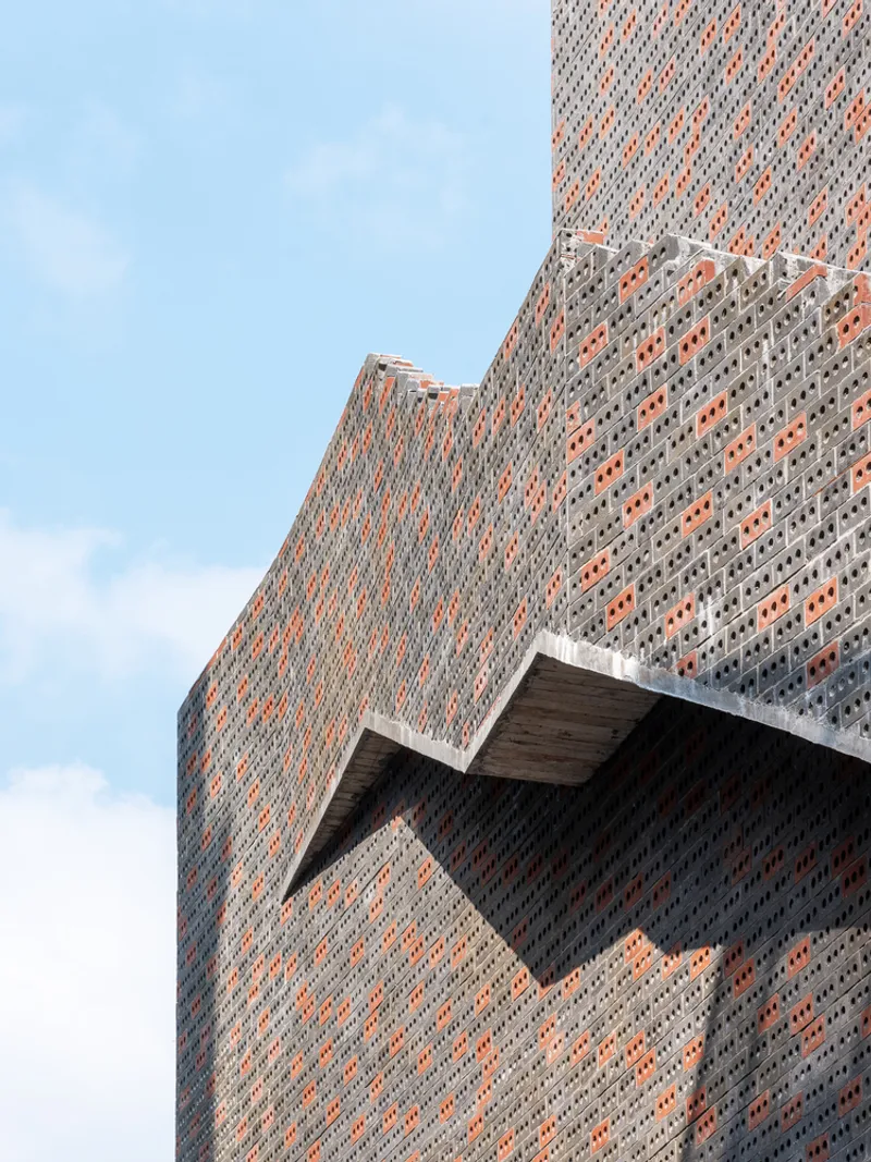 Upward view of projecting brick volume with perforated facade and recessed triangular soffit