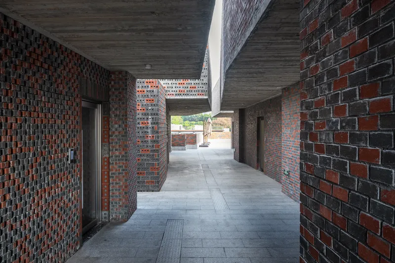 Covered passageway with timber ceiling and variegated brick walls leading to sunlit courtyard