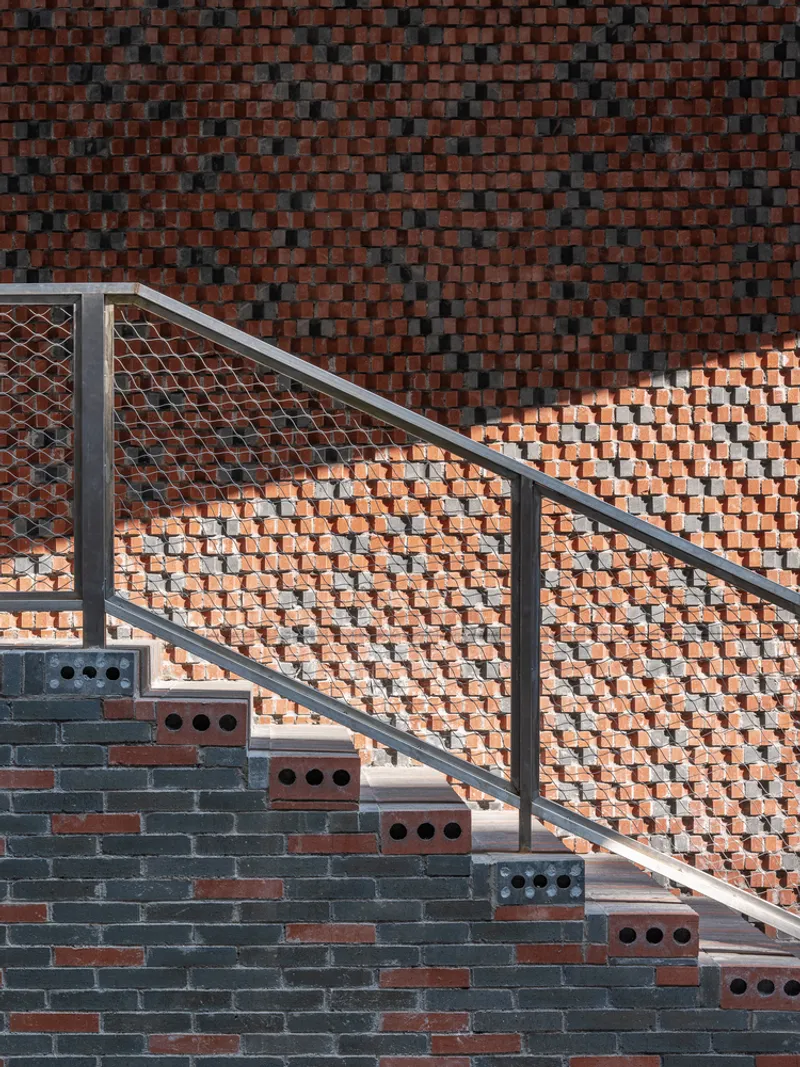 Exterior staircase with metal railing ascending patterned brick walls in afternoon sunlight