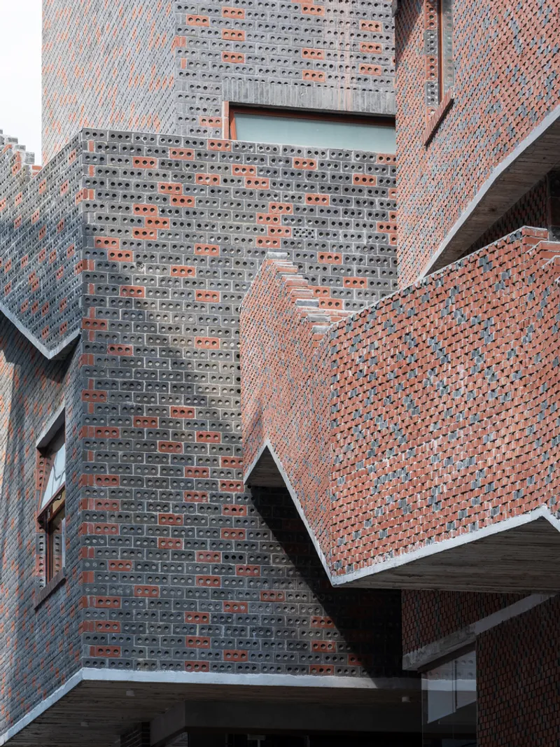 Close-up of perforated gray brick screen walls meeting solid red brick surfaces at angular junctions