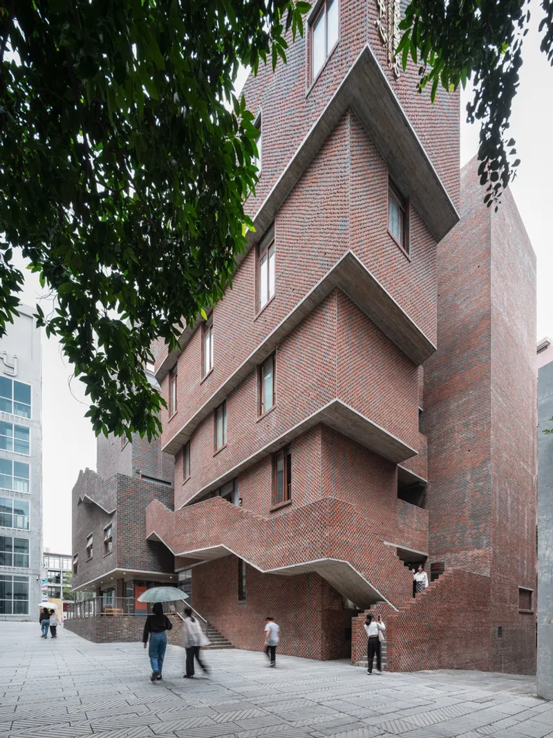 Stacked brick facade with projecting angled volumes framed by overhanging tree branches