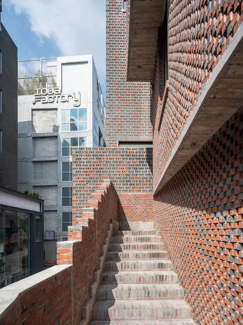 Exterior brick staircase ascending between perforated and solid masonry walls under open sky