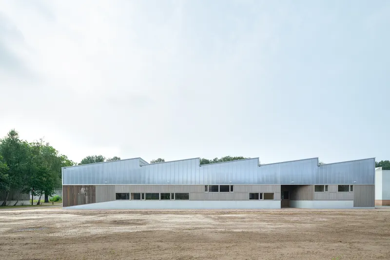 Long view of the horizontal facade with sawtooth roofline and metal cladding edging a gravel yard
