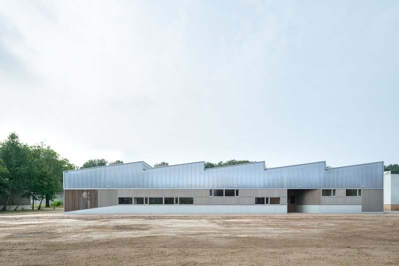 Long view of the horizontal facade with sawtooth roofline and metal cladding edging a gravel yard