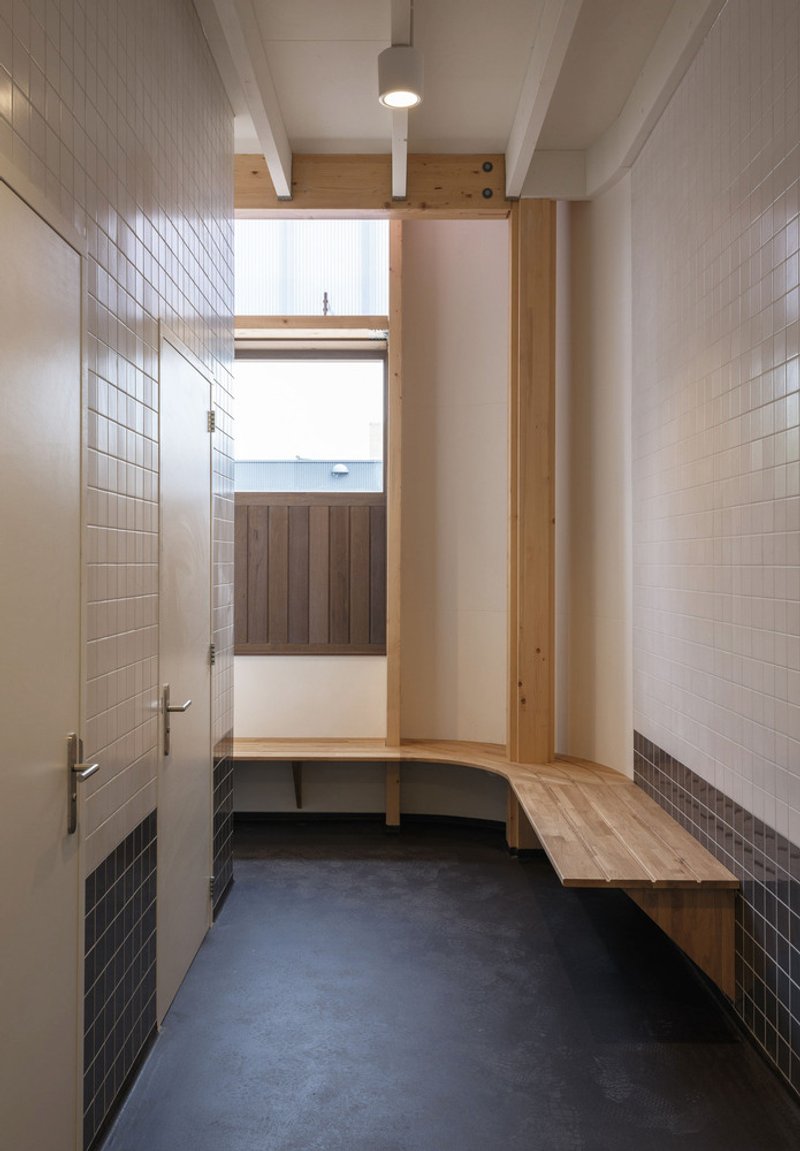 Changing room corridor with white tiled walls, timber bench seating and dark floor tiles