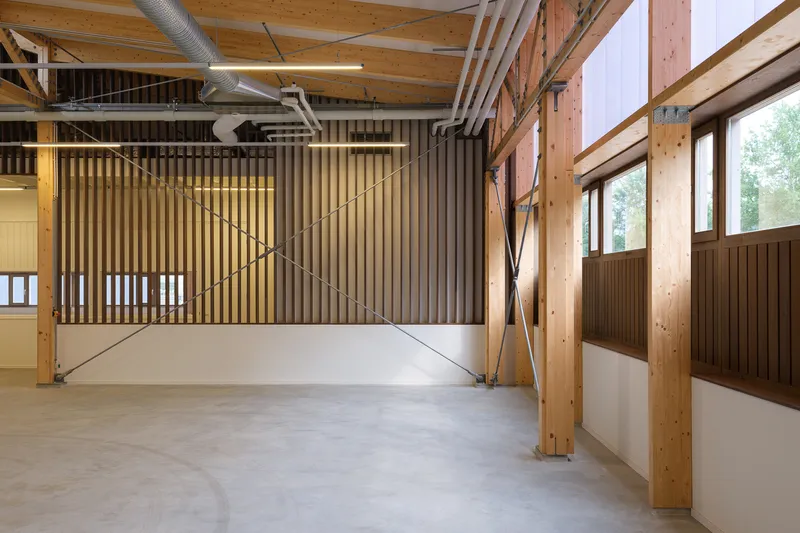 Open workspace with vertical timber slat screen and diagonal steel bracing beneath exposed wooden trusses