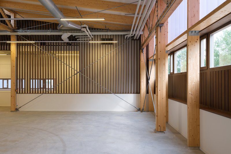 Open workspace with vertical timber slat screen and diagonal steel bracing beneath exposed wooden trusses