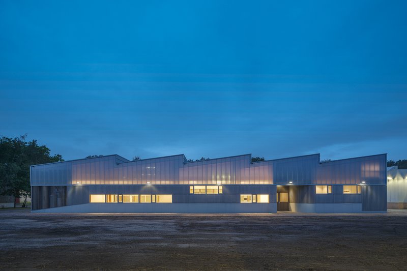 Long street elevation showing the modular roofline and translucent upper clerestory band at evening