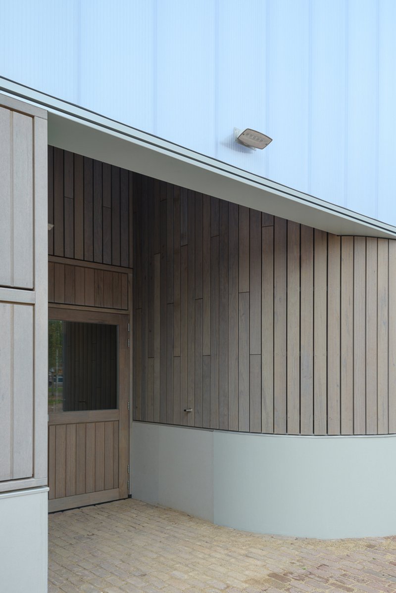 Close-up of curved timber wall meeting white concrete base beneath angled translucent roofline