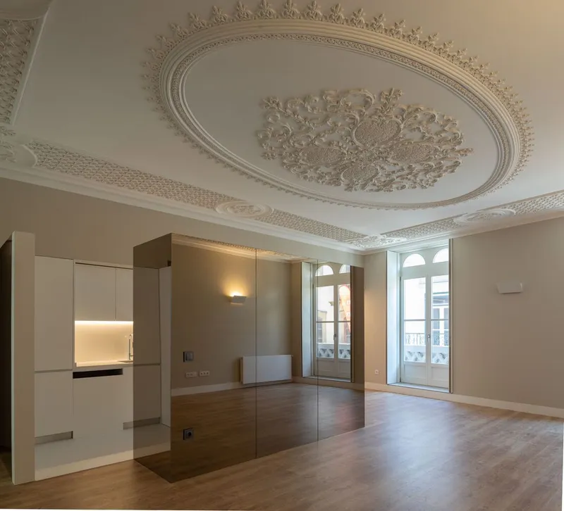 Open plan room with decorative oval ceiling plasterwork, wood flooring and arched balcony doors under natural light