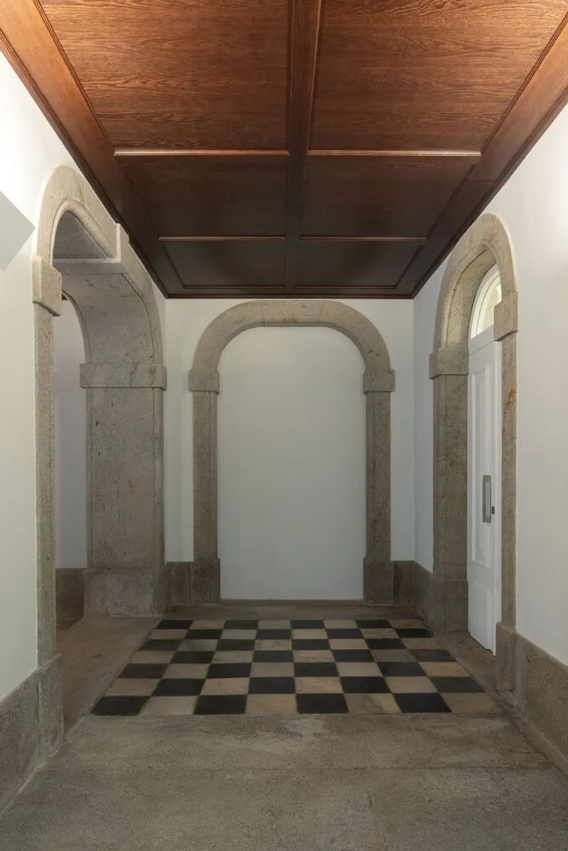 Entrance hall with stone arched doorways, checkerboard floor tile and dark wood paneled ceiling