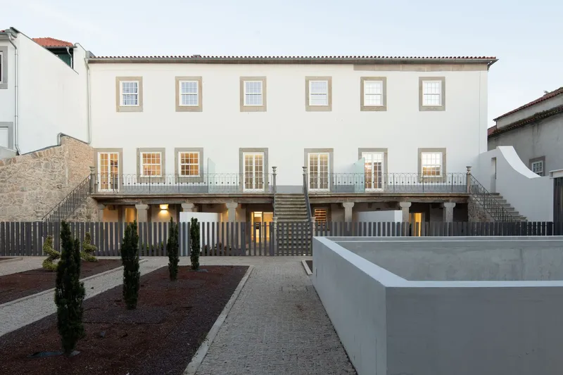 Rear elevation with white facade, stone framed windows and elevated terrace accessible by twin staircases at dusk