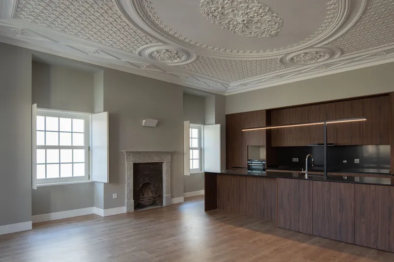 Interior with ornate plaster ceiling medallions, walnut kitchen cabinetry and historic fireplace beneath tall windows