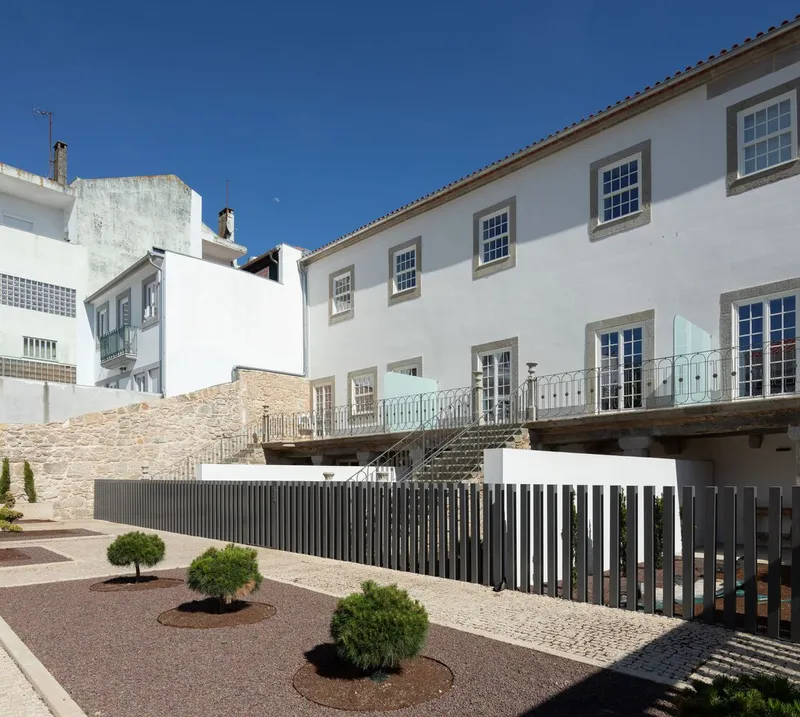 Courtyard view showing stone wall, elevated terrace with metal railings and vertical slat screening under clear sky