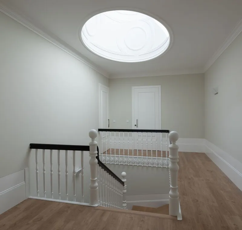 Staircase landing with white painted wood balustrade and circular skylight with decorative molding above