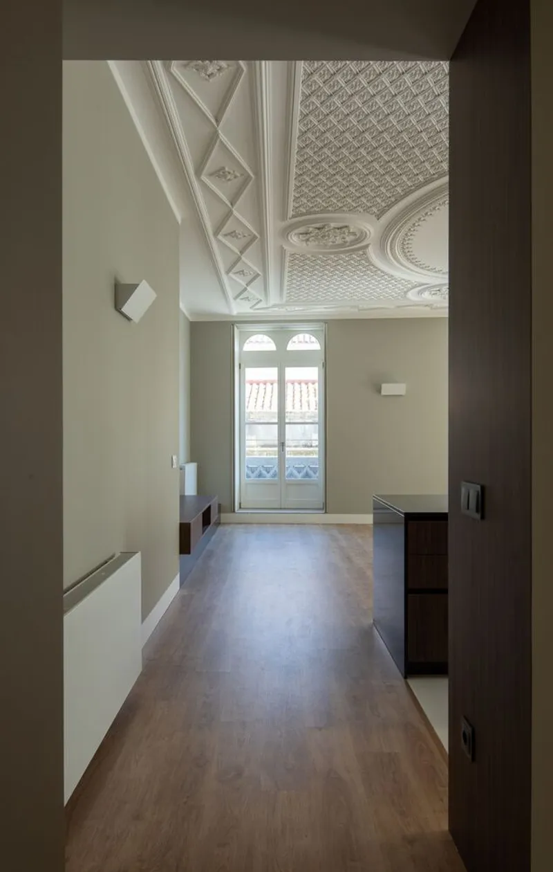 Hallway view toward arched window with ornamental plaster ceiling and wooden flooring in daylight