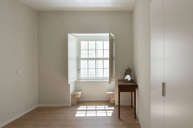 Small room with deep-set window casting gridded shadows across pale wooden flooring and white walls