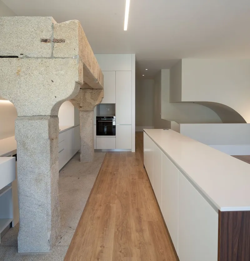 Kitchen with exposed stone column, white cabinetry, and wood flooring beneath a linear ceiling light