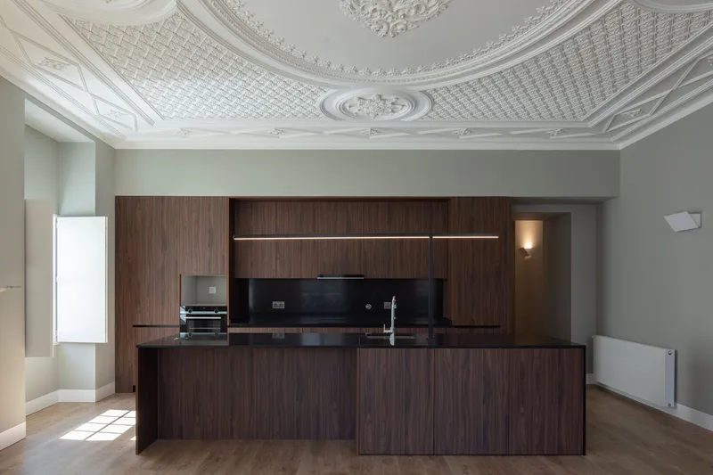 Walnut kitchen island beneath ornate plaster ceiling with geometric and floral relief patterns