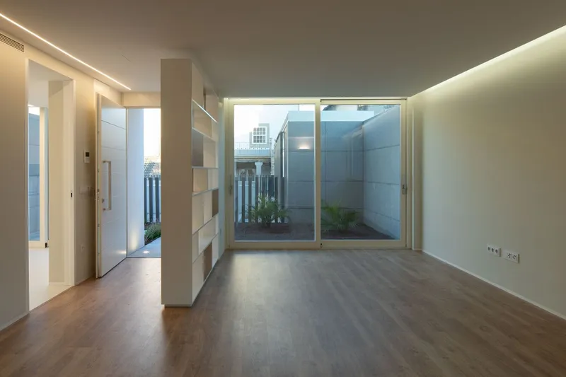 Interior room with wood flooring and built-in shelving facing a glass door overlooking a planted courtyard