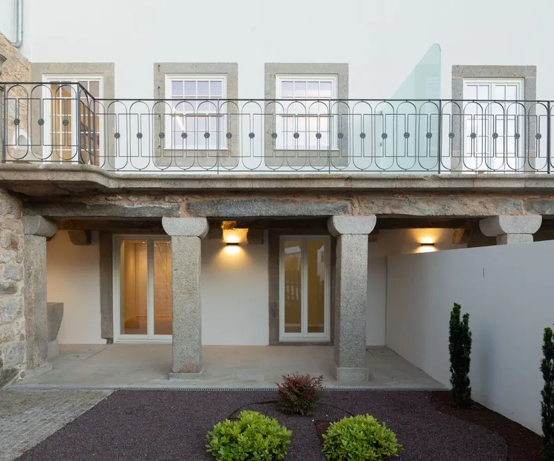 Courtyard facade with granite columns supporting a balcony with ornamental iron railing at dusk