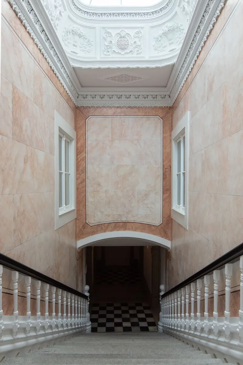 Stairwell with restored plasterwork ceiling and marbled wall finish above a chequered floor