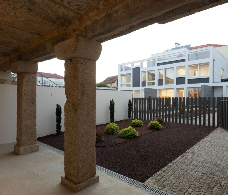View through granite colonnade to landscaped courtyard with dark timber screening and white facade beyond