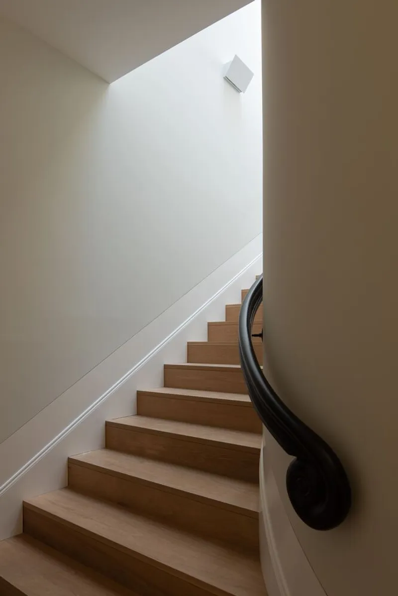 Curved timber staircase with black metal handrail ascending through a skylit stairwell