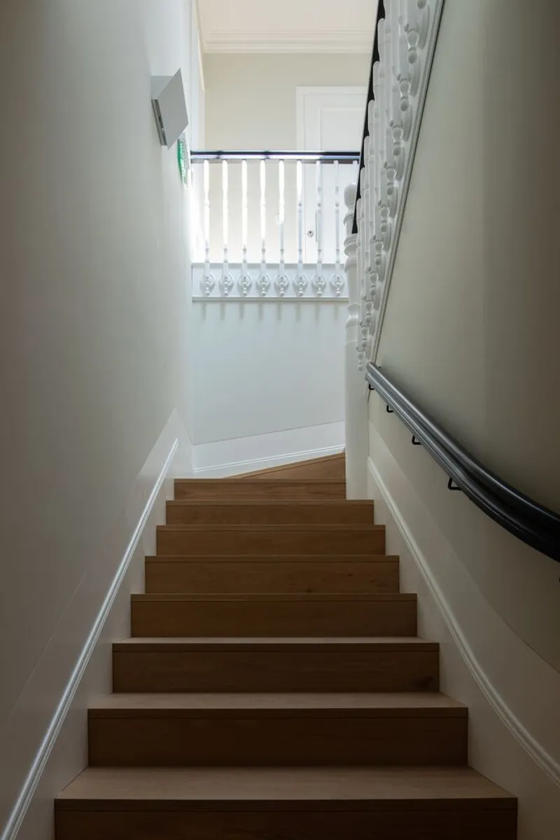Wooden stairs leading upward to a landing with white painted balustrade and natural light