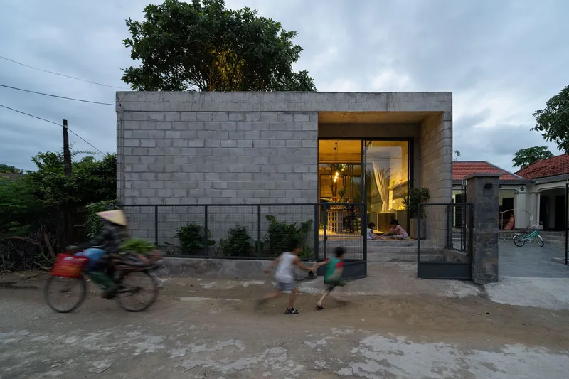Street view of the concrete block facade with recessed entrance as motorbikes and pedestrians pass