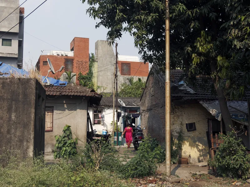 Street context: the brick house rising above the older low-rise neighbourhood, utility poles, figure walking in the lane