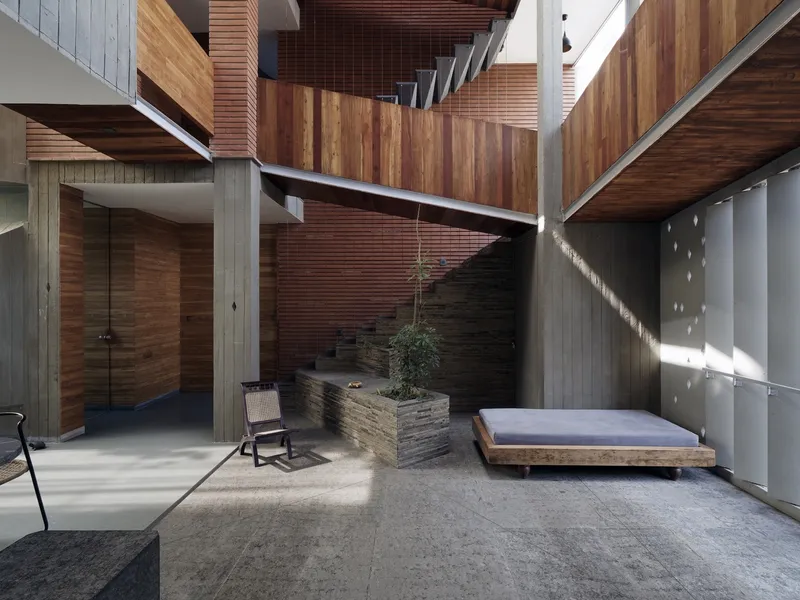 Central courtyard from above: brick and concrete walls, rough stone staircase, timber screens, daybed and chair, open to sky