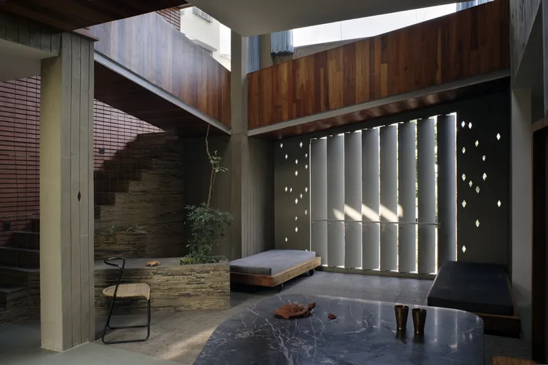 Courtyard at ground level: stone stair, timber daybed, perforated concrete screen casting scattered light dots, brick and timber upper floors