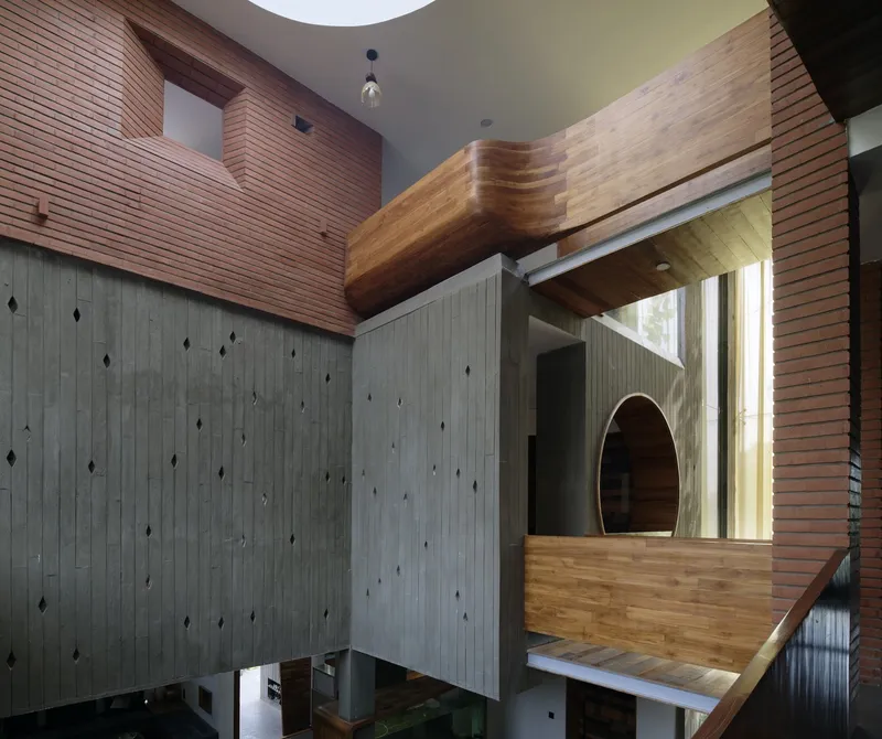 Looking up through the courtyard: concrete columns, brick volumes, timber balcony overhanging, circular oculus, arched timber opening