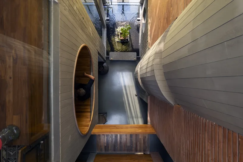 Side corridor: two large circular timber-lined barrel openings set into corrugated metal walls, plant at the far end