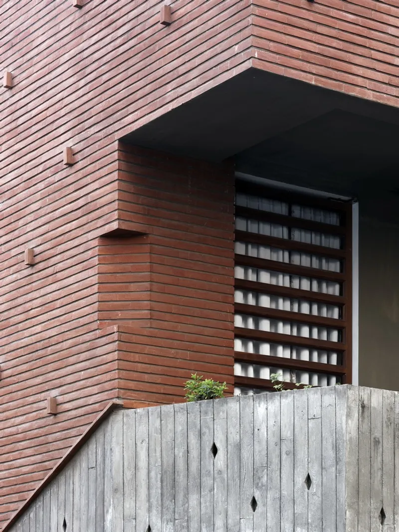 Exterior detail: brick facade with horizontal coursing, board-formed concrete base, brick jaali screen panel