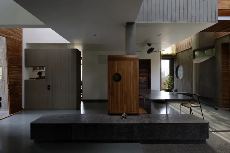 Kitchen and living: dark polished stone counter, timber cabinet with circular handle, vaulted white ceiling, open plan
