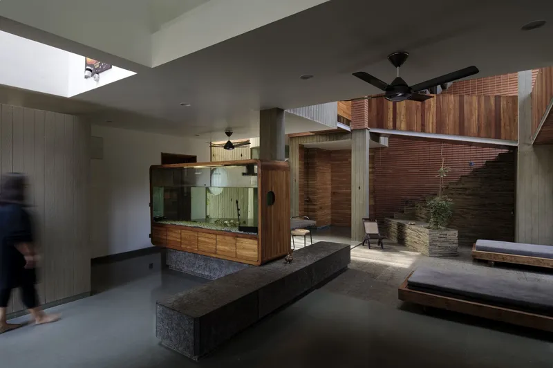 Living area: large glass aquarium on stone plinth, concrete bench seating, ceiling fan, brick staircase visible, blurred figure