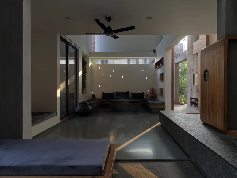 Sitting room: dark polished stone floor, black cushioned seating, perforated wall with scattered light dots, timber cabinet