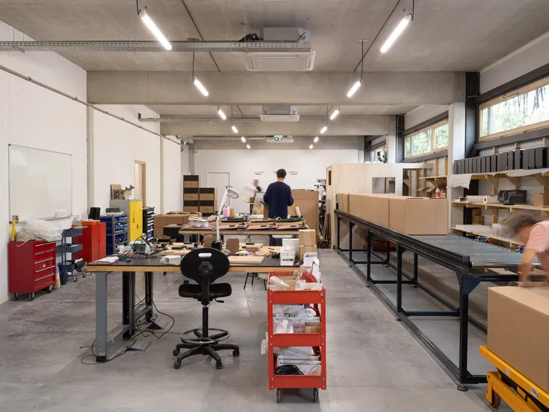 Workshop space with people moving past workbenches loaded with materials and cardboard samples
