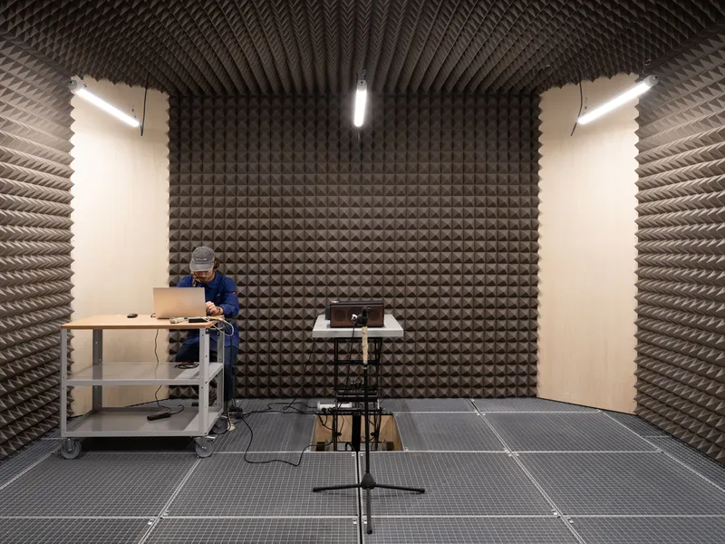 Sound testing chamber lined with pyramidal acoustic foam panels and a person examining equipment at a workbench