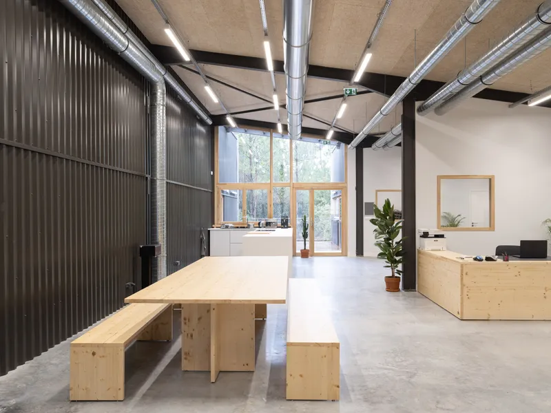 Open communal area with timber dining table and benches, exposed ductwork, and corrugated metal partition wall
