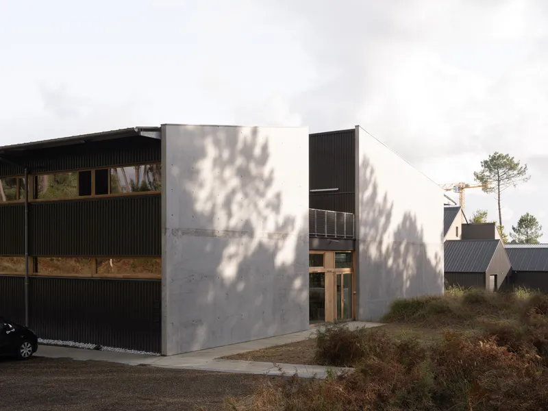 Concrete and corrugated metal facade with dappled tree shadows falling across the entrance wall